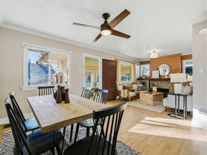 Dining space featuring a fireplace, healthy amount of natural light, wood finished floors, ornamental molding, and a ceiling fan