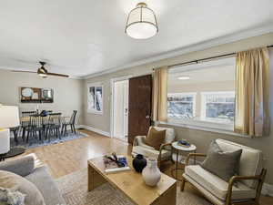 Living area featuring plenty of natural light, wood finished floors, a ceiling fan, and crown molding