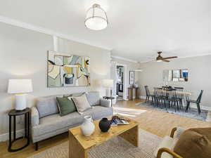 Living area with light wood-style flooring, ornamental molding, and a ceiling fan