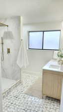 Full bath featuring double vanity, a marble finish shower, a textured ceiling, and light flooring