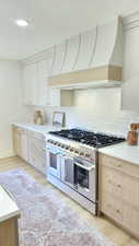 Kitchen with double oven range, a textured ceiling, light wood finished floors, custom exhaust hood, and tasteful backsplash