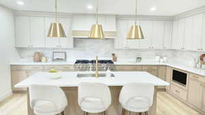 Kitchen featuring light brown cabinets, hanging light fixtures, decorative backsplash, light wood-type flooring, and recessed lighting