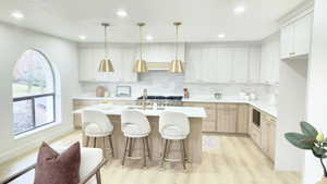 Kitchen with a kitchen bar, light wood-style floors, a kitchen island with sink, backsplash, and pendant lighting