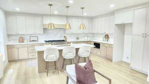 Kitchen with a breakfast bar, light wood-style floors, hanging light fixtures, an island with sink, and recessed lighting