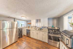Kitchen featuring appliances with stainless steel finishes, dark wood-type flooring, a textured wall, white cabinets, and a textured ceiling