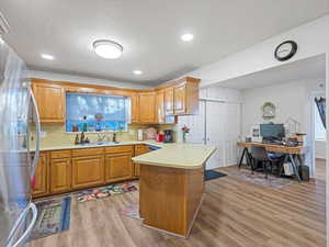 Kitchen featuring light countertops, a peninsula, freestanding refrigerator, brown cabinetry, and light wood-type flooring