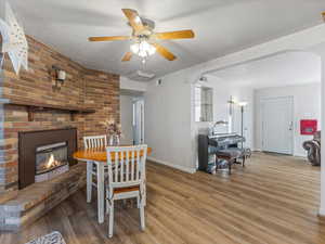 Dining area with a brick fireplace, wood finished floors, arched walkways, and a ceiling fan