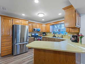 Kitchen with a peninsula, appliances with stainless steel finishes, light countertops, light wood finished floors, and recessed lighting