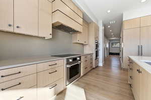 Kitchen with light brown cabinets, custom range hood, modern cabinets, and recessed lighting