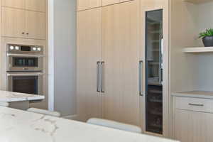 Kitchen with light brown cabinets, stainless steel double oven, modern cabinets, light stone countertops, and open shelves