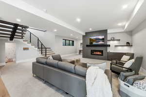 Living room with stairs, a large fireplace, and recessed lighting
