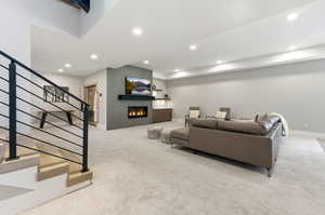 Living area featuring stairs, a glass covered fireplace, recessed lighting, and light colored carpet