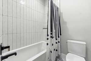Bathroom featuring toilet and shower / bathtub combination with curtain