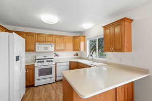 Kitchen with white appliances, a peninsula, light countertops, and brown cabinetry