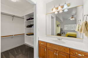 Bathroom with vanity, dark colored carpet, connected bathroom, ceiling fan, and a spacious closet