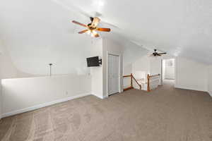 Additional living space featuring a ceiling fan, carpet, a textured ceiling, and lofted ceiling