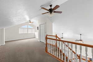 Corridor with vaulted ceiling, carpet flooring, a textured ceiling, and an upstairs landing
