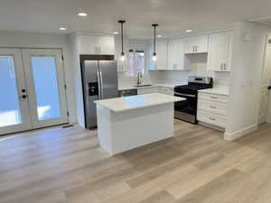 Kitchen featuring appliances with stainless steel finishes, white cabinets, a kitchen island, light wood finished floors, and recessed lighting