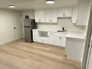 Kitchen with white cabinets, freestanding refrigerator, light wood finished floors, and light stone counters