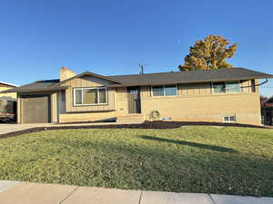 Ranch-style home featuring brick siding, a front lawn, board and batten siding, an attached garage, and driveway