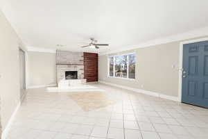 Unfurnished living room with crown molding, a large fireplace, ceiling fan, and light tile patterned flooring