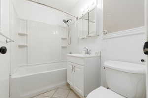 Full bathroom with vanity, tub / shower combination, light tile patterned floors, and a wainscoted wall