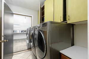 Washroom featuring a textured ceiling, cabinet space, washing machine and clothes dryer, light tile patterned floors, and a wall unit AC