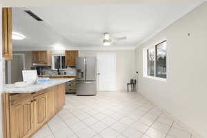Kitchen with brown cabinetry, ornamental molding, stainless steel fridge with ice dispenser, a ceiling fan, and light stone counters