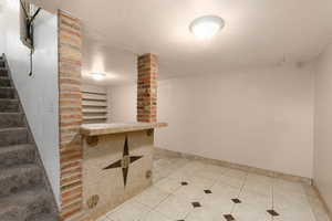 Finished below grade area with light tile patterned floors, stairway, and a textured ceiling