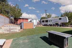 View of green lawn with a storage unit and a patio