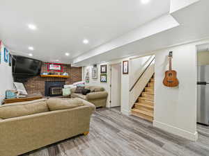 Living room featuring wood finished floors, stairs, a wood stove, recessed lighting, and brick wall