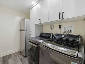 Laundry room with light wood-style flooring, separate washer and dryer, and cabinet space