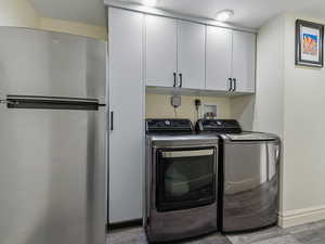 Laundry area featuring washing machine and clothes dryer, cabinet space, and light wood-style floors