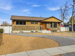 View of front of home featuring stone siding, a shingled roof, and a gate