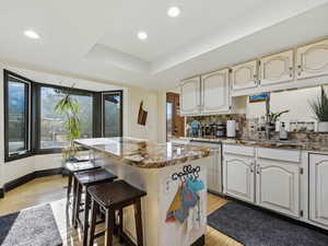 Kitchen featuring a kitchen bar, dark stone counters, a center island, tasteful backsplash, and a tray ceiling