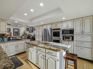 Kitchen with a center island, a raised ceiling, light stone counters, stainless steel appliances, and recessed lighting