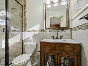 Bathroom with vanity, tile walls, a stall shower, and wainscoting