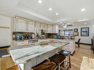 Kitchen with a breakfast bar, a tray ceiling, light wood-style flooring, light stone countertops, and a kitchen island
