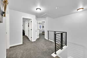Hallway with an upstairs landing, attic access, carpet flooring, and a textured ceiling