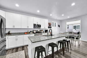 Kitchen featuring dark stone countertops, white cabinets, appliances with stainless steel finishes, a breakfast bar, and dark wood finished floors