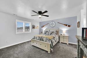 Bedroom with dark carpet, a ceiling fan, a warm lit fireplace, and a textured ceiling