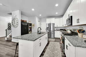 Kitchen featuring stainless steel appliances, light stone counters, a kitchen breakfast bar, white cabinets, and a kitchen island with sink