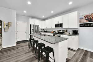 Kitchen with appliances with stainless steel finishes, a kitchen bar, dark stone countertops, white cabinets, and a center island with sink
