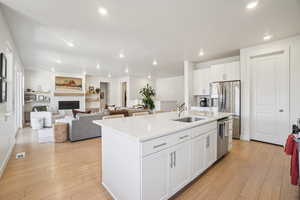 Kitchen featuring white cabinets, light wood-style flooring, a kitchen island with sink, stainless steel appliances, and open floor plan