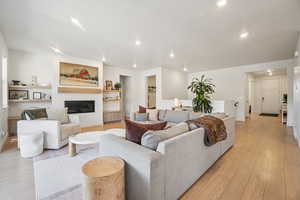 Living area with light wood-style floors, a glass covered fireplace, and recessed lighting