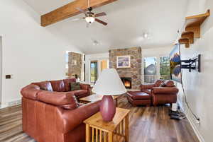 Living area featuring a stone fireplace, wood finished floors, ceiling fan, beamed ceiling, and high vaulted ceiling