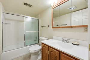 Full bath with vanity, enclosed tub / shower combo, and a textured ceiling