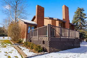Snow covered back of property with a wooden deck, a chimney, and brick siding