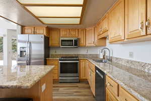 Kitchen featuring stainless steel appliances, light stone countertops, light wood-type flooring, and a textured ceiling