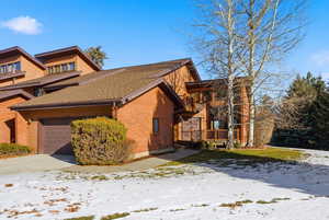 Snow covered property featuring an attached garage, a shingled roof, and brick siding